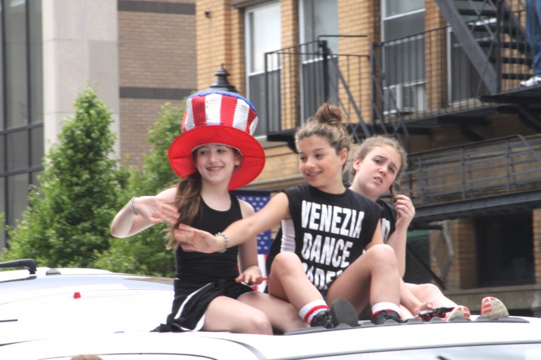 Girls from the Venezia Dance Academy wave from the top of a truck.