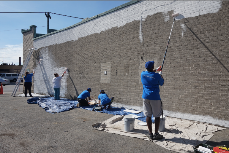 A wall on Bishop's Walk in Watertown Square is being prepped by Tufts volunteers so it can be turned into a mural.