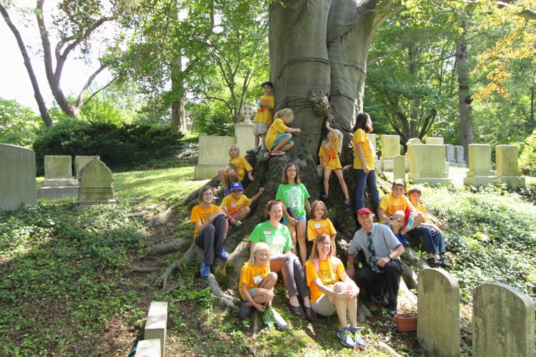 Campers from the Church of the Good Shepherd's Vacation Garden Camp sit on the roots of a tree at Mount Auburn Cemetery.