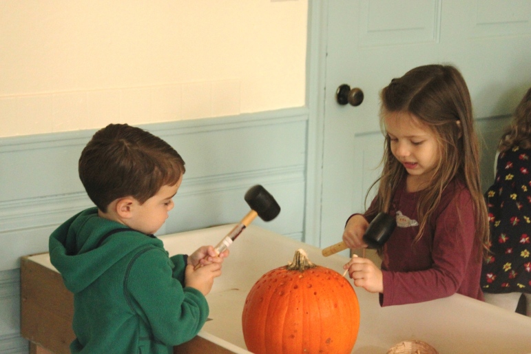 Children hammer pegs into a pumpkin at one of the activity stations at Russell Cooperative Preschool.