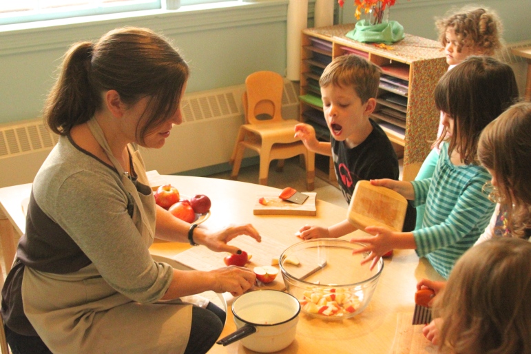 Russell Cooperative Preschool teacher Jenna Rounds helps students cut apples for their apple sauce snack.