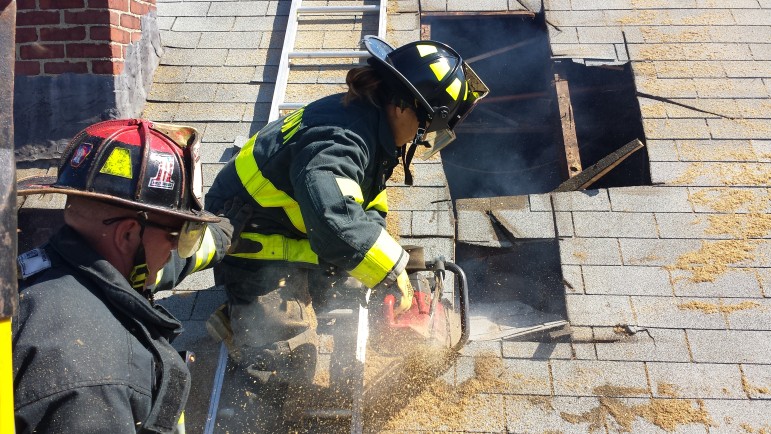 Lt. Dan Lavache watches as newly appointed firefighter Anna Pelevina uses a saw to cut into the roof of a home on Harrington Street due to be demolished that the Fire Department was allowed to use for training.
