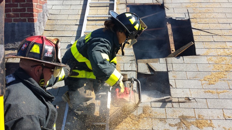 Lt. Dan Lavache watches as newly appointed firefighter Anna Pelevina uses a saw to cut into the roof of a home on Harrington Street due to be demolished that the Fire Department was allowed to use for training.