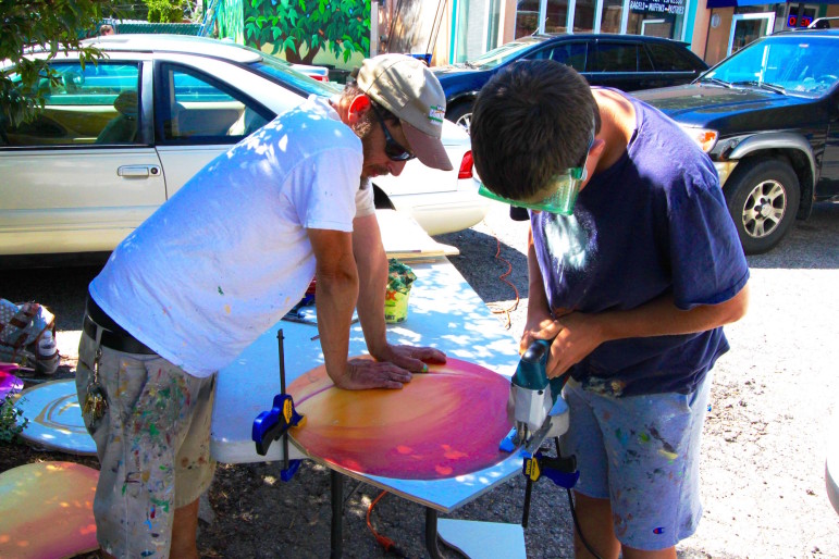 Artist Gregg Bernstein worked on his third mural with Watertown High School students this summer. Here he helps a student cut out a fruit painted on wood that will go in a storefront. 