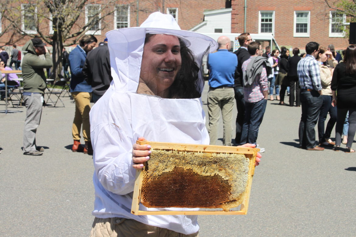 A visitor tries on a bee keeping outfit and takes a look at a section of honeycomb from a bee hive at the Bee Bandits table.
