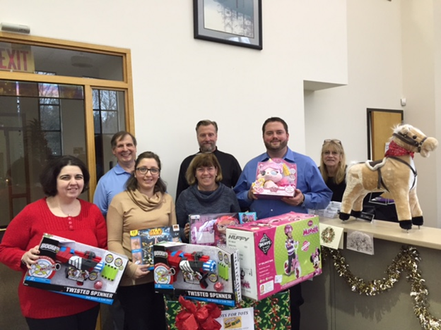 The H&K Insurance staff with stands with some of the gifts collected for Toys for Tots in 2015. 